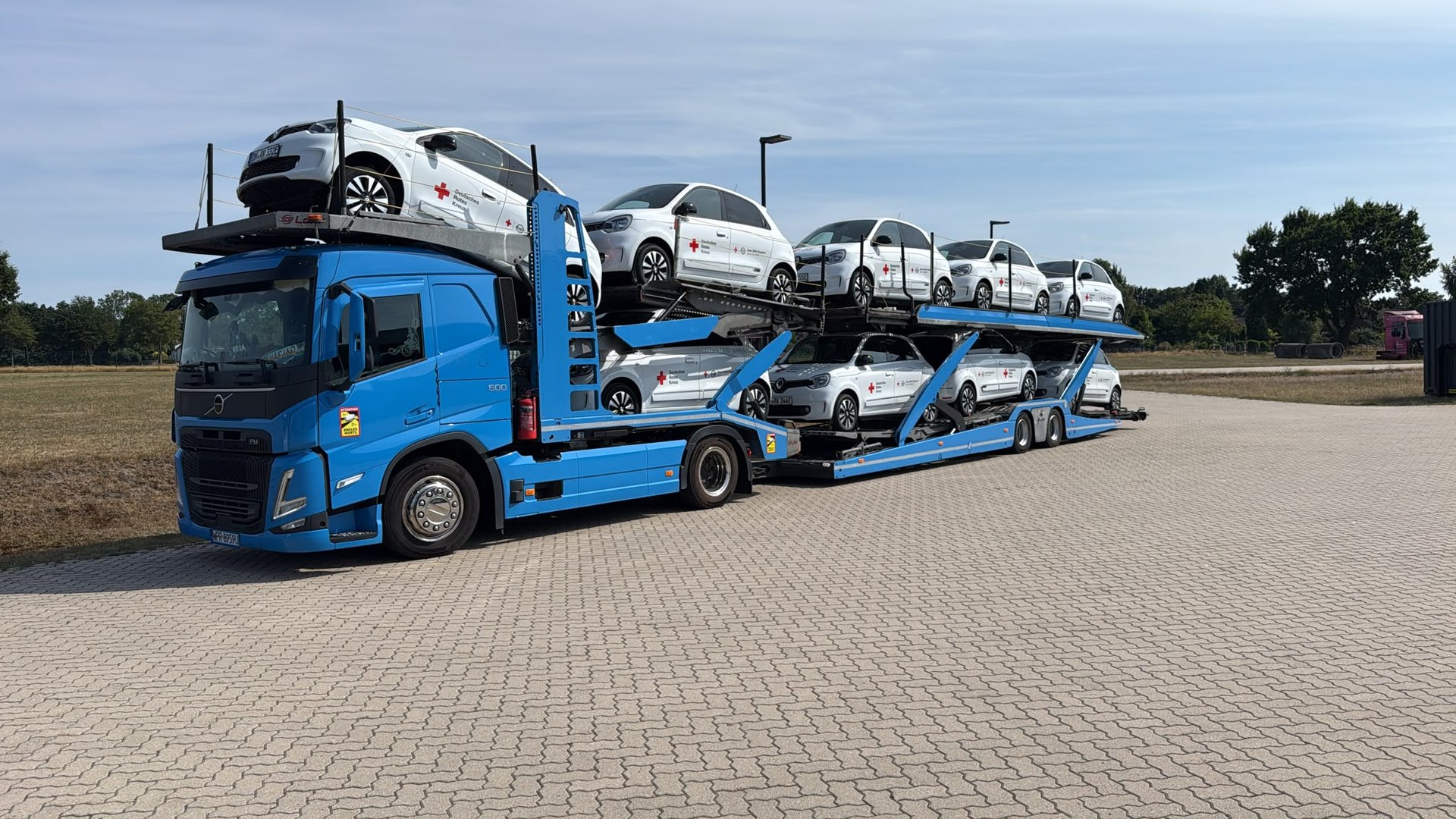 Niebieski autotransporter MotoLogix Volvo załadowany białymi autami miejskimi